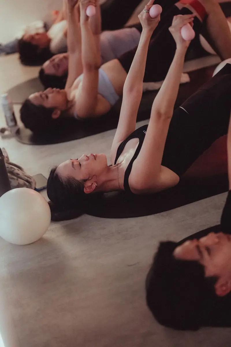 A class on mats lifting pilates balls, seen from above