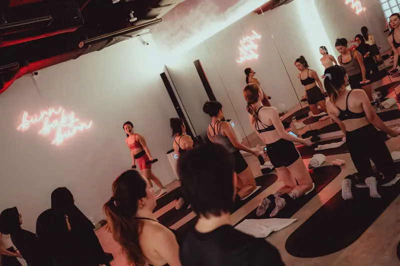 A hot mat class kneeling on mats with hand weights under pink neon signs