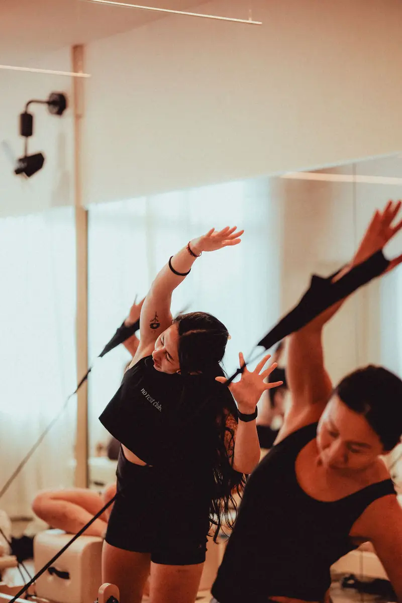 Two women side-bending with reformer straps, arms raised