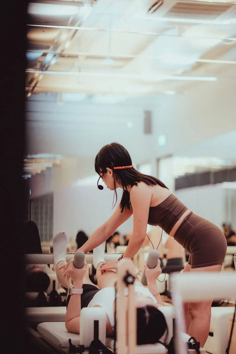 An instructor with a headset adjusting a reformer for a client