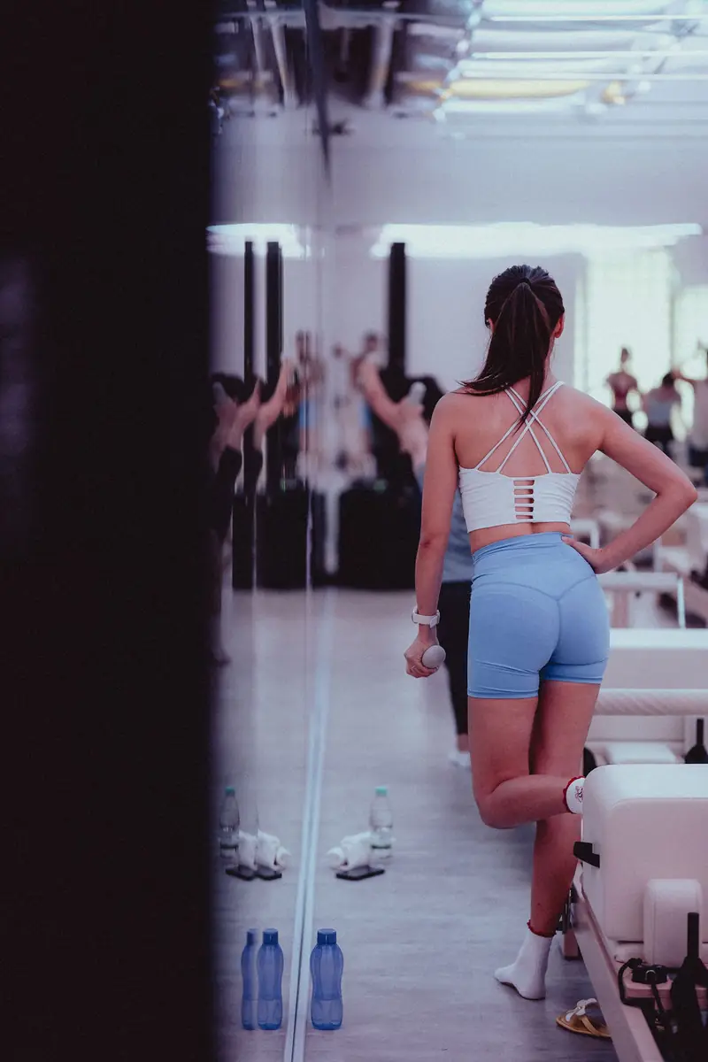 A woman in blue shorts between reformers in a mirrored room