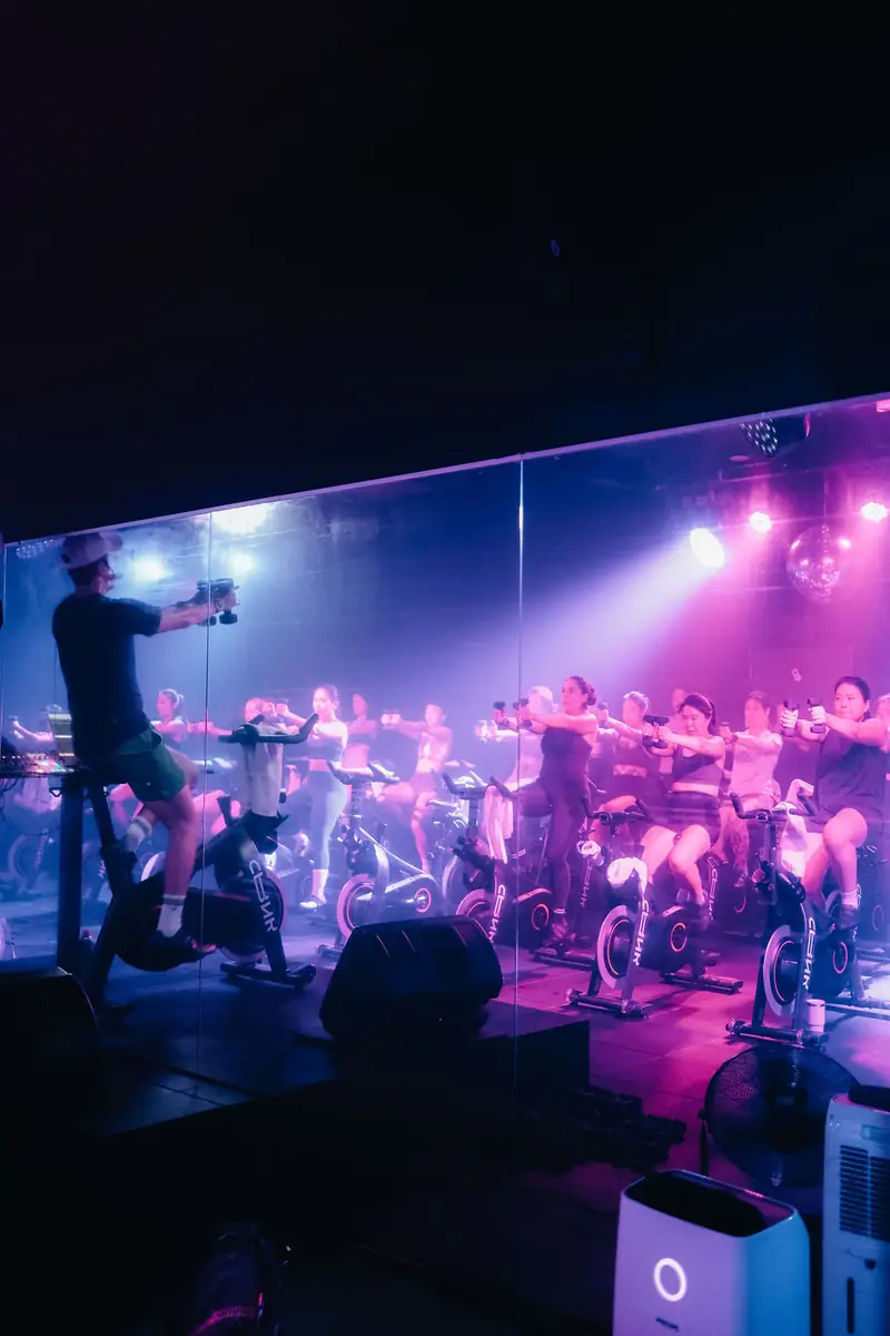 An instructor on the podium leading a full room under purple and pink lights