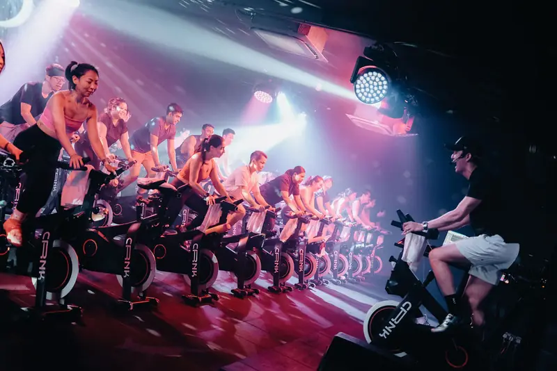 A packed CRNK Ride class under red and pink lights, instructor up front